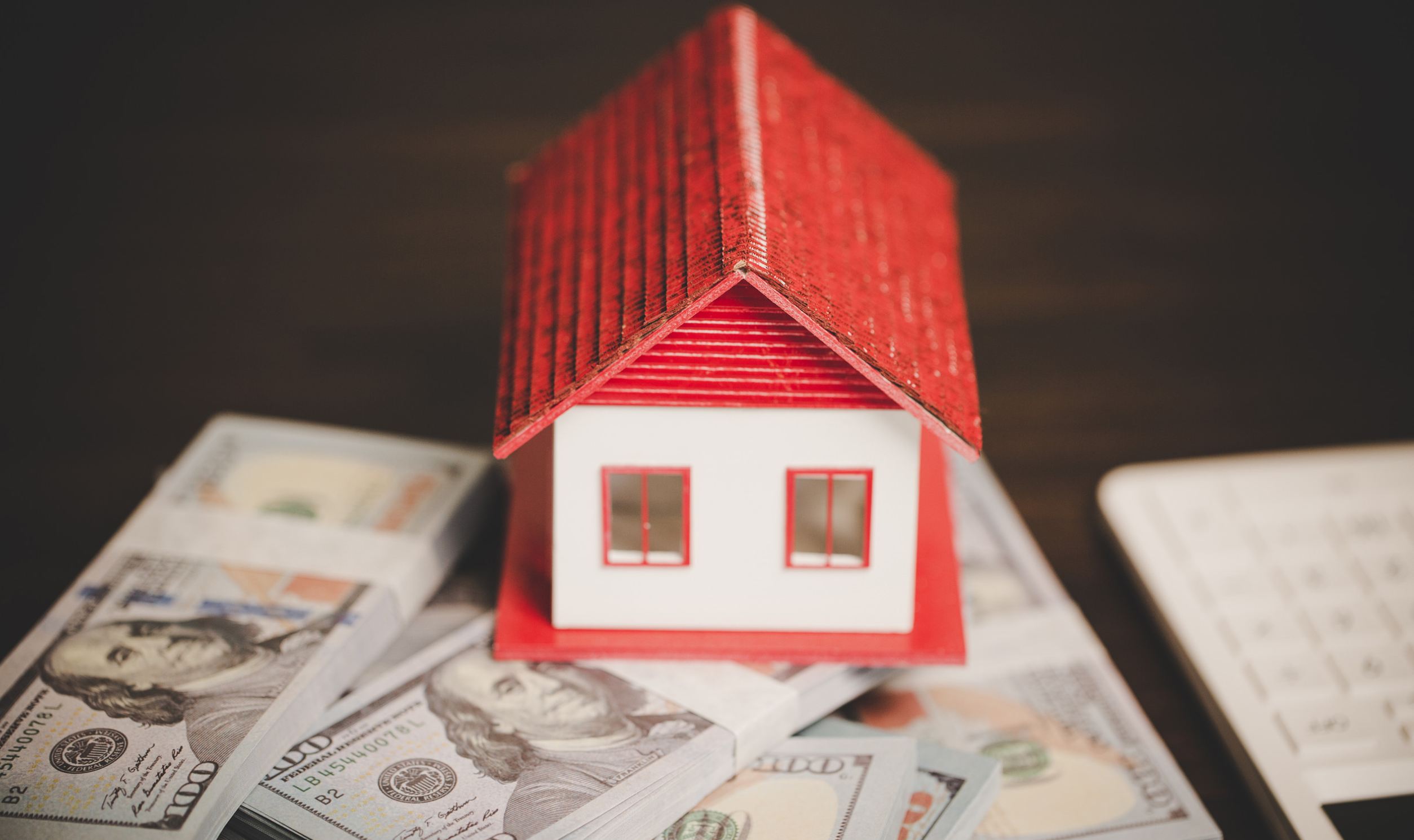 Focus house model on blur real estate agent and buyer background. Enthusiastic Model house on stacks of hundred-dollar bills, symbolizing mortgage financing and home purchase options.