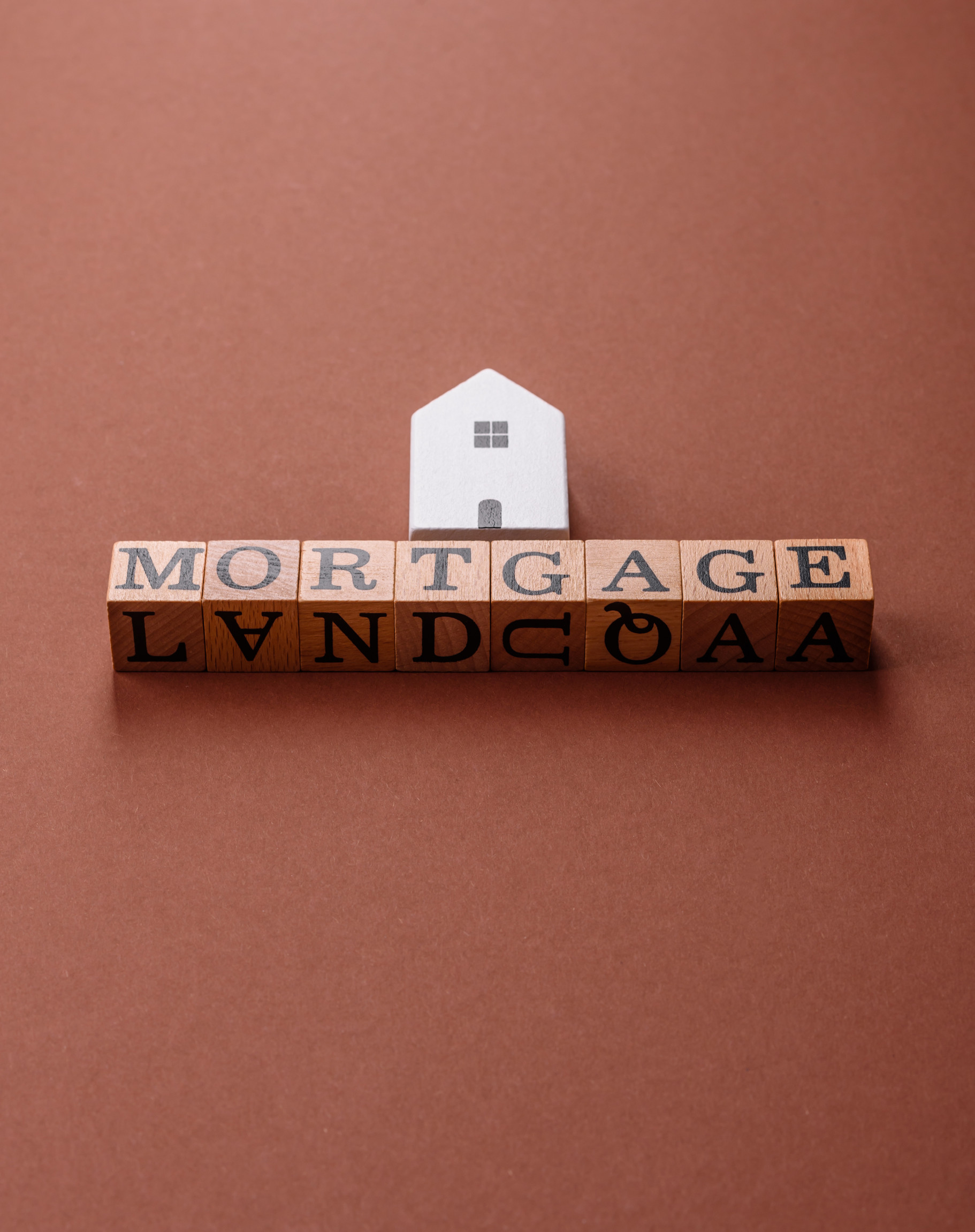 House, real estate or property bought with a mortgage, purchase or sale of apartments Mortgage blocks with a small house figurine on a brown background, symbolizing home financing and mortgage services offered by American Liberty Mortgage.
