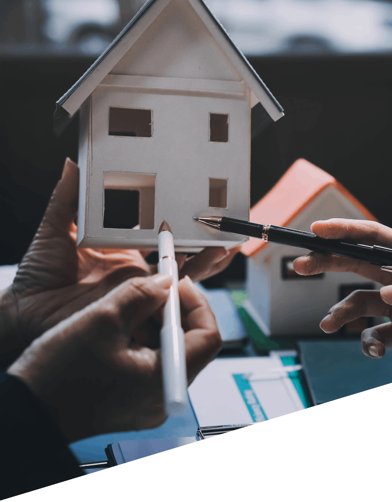 Hands holding a model house, discussing home financing options with pens and markers, symbolizing the mortgage guidance offered by American Liberty Mortgage in Victoria, TX.