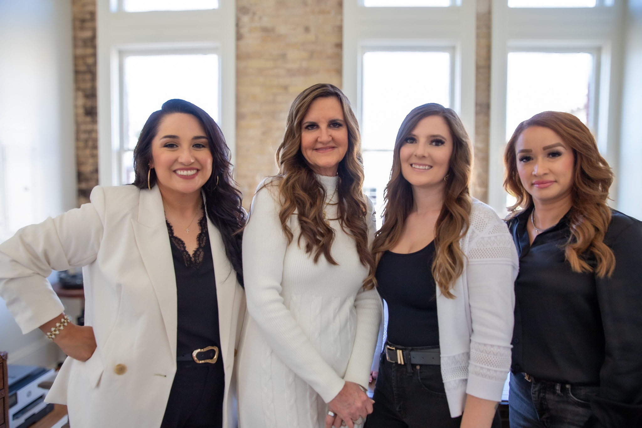 Four professional women smiling together in a bright, modern office setting, representing the American Liberty Mortgage team in Victoria, TX, emphasizing local expertise and personalized mortgage solutions.